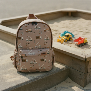 Kinderrucksack building machines am Rand eines Sandkastens mit Spielzeugbaggern